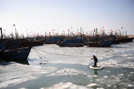 A fisherman takes raft to board a ship at Sanshandao Fishing Port of Laizhou City, east China's Shandong Province, Jan. 15, 2010. 