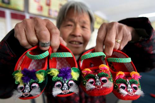An old granny shows her hand-made embroidered shoes at Guanzhuang Village, Wenxi County, north China's Shanxi Province, Jan. 19, 2010. With the approaching of the Year of Tiger according to traditional Chinese lunar calendar, local villagers start making varieties of delicate ornamental articles for the Spring Festival. [Xinhua photo]