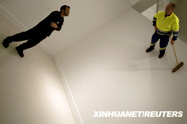 A man looks at German artist Johan Lorbeer (R) attached to a wall during his performance &apos;Proletarisches Wandbild&apos; at the Contemporary Art Center in Malaga, southern Spain, January 20, 2010. [Xinhuanet/Reuters]