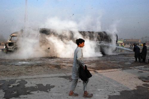 A man passes by a burned oil tanker truck on the outskirts of Peshawar, city of northwest Pakistan, Jan. 23, 2010. An oil tanker truck of NATO was attacked by unidentified militants on Saturday.