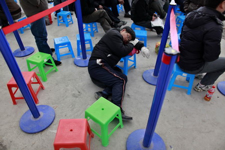 A passenger rests on a small stool as he waits to buy train tickets at the Shanghai Railway Station January 26, 2010.[China Daily via Agencies]