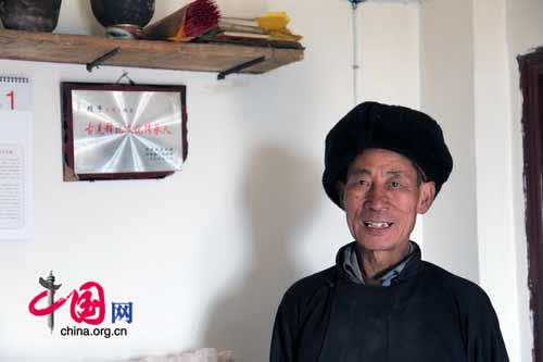 The only surviving Shibi in Luobo Village, Wang Mingjie stands in his new home. The plaque says 'The Inheritor of Qiang Shibi Culture.'