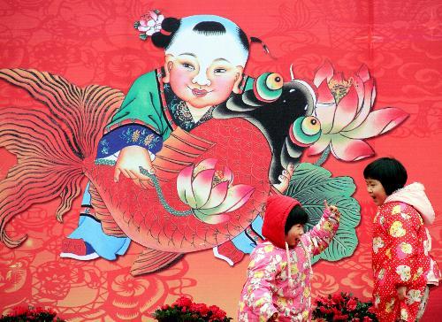 Two kids play in front of a large New Year picture at a New Year picture festival held on the Zhonghua Gate Square in Nanjing, capital of east China's Jiangsu Province, February 1, 2010.