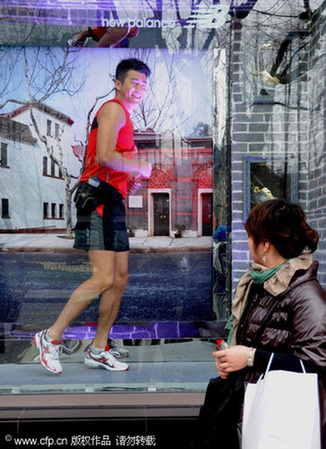 A passer-by watches a model jogging in a window of a sportswear shop in Shanghai, Feb 1, 2010. 