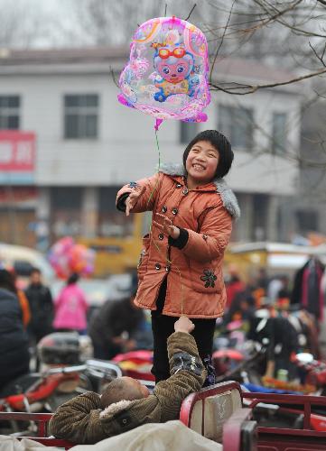 A little girl is joyous at stroking and fondling the toy balloon as local villagers in hustle and bustle throng to the rural bazaar of Spring Festival to select and purchase the new goods for use during the Spring Festival, in Shanting Town, Zaozhuang, east China's Shandong Province, Feb. 2, 2010. (Xinhua/Gao Qiming) 