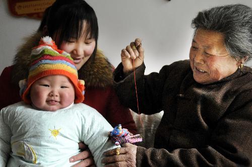 Geng Yiying (R) decorates cloth dolls of Spring Cock onto her grandchild's sleeve in Sangcun Township in Zaozhuang City, east China's Shandong Province, February 4, 2010, the day of Spring begins. [Xinhua photo]