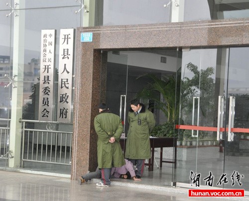 Liao Fuping and Zhu Daguo stand at the entrance to the Kaixian county office building as Yin Xianqiong lies at their feet in this Jan 13 photo taken and posted online by an unnamed netizen. 