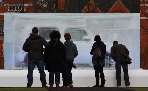 Some tourists look at a giant tattoo ice cube at Potters Fields, close to the Tower Bridge, in London, Feb. 9, 2010. [Xinhua]