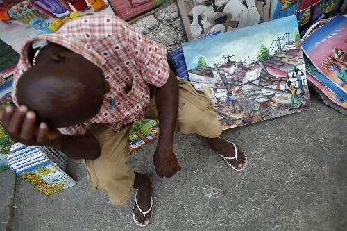 A man sits next to a painting about the earthquake at a street side art market in Petionville, Port-au-Prince February 15, 2010. Some Haitian artists began to write songs or paint frames about the earthquake as a way to express their tragedy.