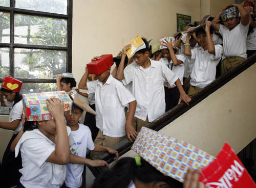 Students use make shift protective head gear and books to cover their heads as they leave a building during an earthquake drill at San Juan elementary school in San Juan, Metro Manila February 17, 2010.