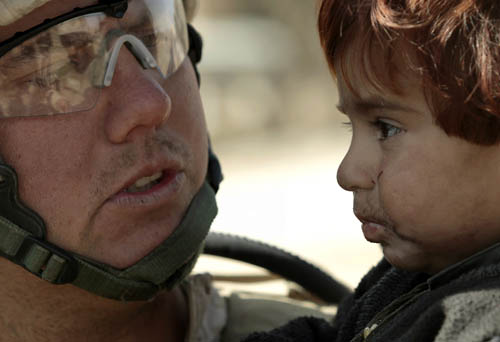U.S. Marine Gunnery Sergeant Brandon Dickinson from Bravo Company of the 1st Battalion, 6th Marines holds a toddler in the town of Marjah, in Nad Ali district of Helmand province February 17, 2010. The Marines were approached by the boy&apos;s father who wanted help for the child&apos;s skin condition. [Xinhua] 