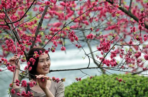 A woman poses for photos with peach blossoms in Guilin, southwest China's Guangxi Province, at a sunny spring day on Feb. 26, 2010. [Xinhua/Chen Ruihua]