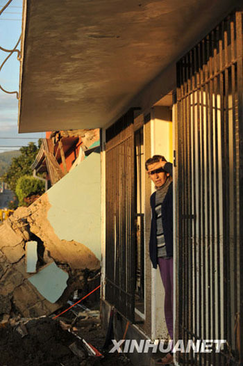 A woman looks out from the doorway of her house in Constitución, a town 450 km south of Chilean capital Santiago on March 2, 2010.[Song Weiwei/Xinhua] 