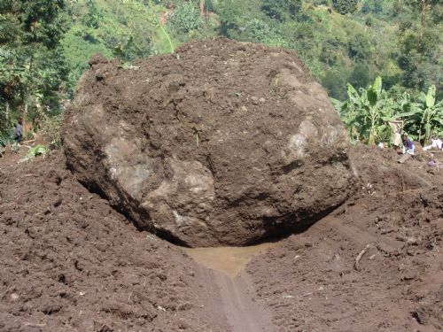 A huge rock lies on the ground as rescuers nearby search for survivors and victims of the landslide at Nametsi village in Bududa District, about 370 kilometers east of the Ugandan capital Kampala, on March 3, 2010. Soldiers and villagers in eastern Uganda hacked at mounds of thick mud with picks and hoes on Wednesday in a desperate bid to find more survivors from the landslide that killed at least 77 people and left over 250 missing. [Julius Odeke/Xinhua]