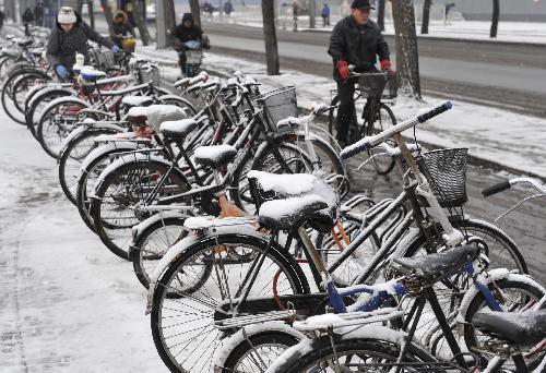Local residents ride past snow-coated bicycles in Beijing, March 8, 2010. Snowfall began hitting the Chinese capital Sunday night and is continuing to fall Monday morning. [Xinhua]