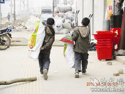 Two pupils in Wuhan collect garbage to stuff in a big plastic bag on Saturday, March 13, 2010. [Photo: cnhubei.com] 