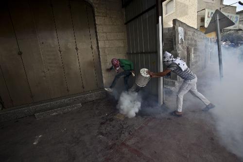 Palestinian protesters tries to deactivate a tear gas canister during clashes at Qalandiya checkpoint near the West Bank city of Ramallah on March 17, 2010. Clashes erupted to protest against Israeli consecrating a synagogue in the old city of Jerusalem. .[Mamoun Wazwaz/Xinhua] 
