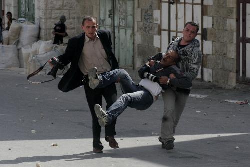 Palestinians carry a wounded photographer during clashes with Israeli soldiers in the West Bank city of Hebron on March 17, 2010. Clashes erupted to protest against Israeli consecrating a synagogue in the old city of Jerusalem.[Mamoun Wazwaz/Xinhua]