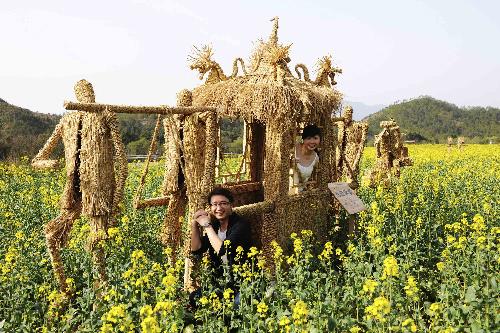 Tourists pose for a photo beside straw men in the cole field at the Shenxianju scenic area in Taizhou City, east China's Zhejiang Province, March 18, 2010.