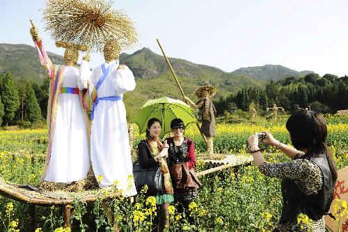 Tourists pose for a photo beside straw men in the cole field at the Shenxianju scenic area in Taizhou City, east China's Zhejiang Province, March 18, 2010.