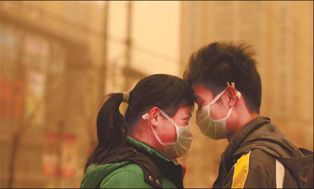 A couple gets close despite their facemasks in the streets of Beijing. The city experienced its second sand storm on Monday. [China Daily]