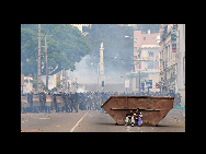 Two supporters of Antananarivo Mayor Andry Rajoelina take refuge behind a container as the police fire tear gas after a rally in the main avenue of the Madagascan capital Antananarivo, on Feb. 16, 2009. Around 10,000 proptestors had gathered at the city's main square for a rally in support of Antananarivo's sacked mayor Andry Rajoelina who has called for the removal of President Marc Ravalomanana. [China Daily/CHIPP Organizing Committee] 