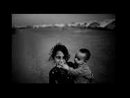 A young girl, internally displaced due to the Pakistan Army's offensive against the Taliban in Swat, looks on as her brother puts a block of ice in her mouth at the Yar Hussain relief camp in Chota Lahore on May 20, 2009 in Swabi, Pakistan. Over 3 million people were believed to have been displaced as a result of military operations against the Taliban in Pakistan. [China Daily/CHIPP Organizing Committee]