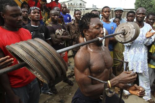 People watch as a man lifts a bar containing 50 kg (110 lbs) iron weights with his mouth at an open gym in Lagos March 27, 2010.