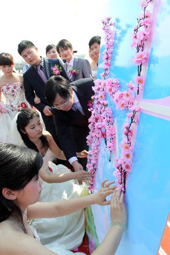 Bridegrooms and brides stick the peach blossom twigs onto the screen to form a pattern, during a collective wedding on the title of Love at Grassroot and Affection Devoted at Yaozhuang Village, in which 18 pairs of graduates-turned-village cadres swear in their matrimony, on the Peach Blossom Island in Yaozhuang Town, Jiashan County, east China's Zhejiang Province, March 28, 2010. (Xinhua/Hu Lingxiang)