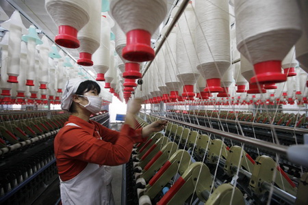 This picture taken in February shows a worker operating a spinning machine at Qixin Textile Mill in Huaibei, Anhui.
