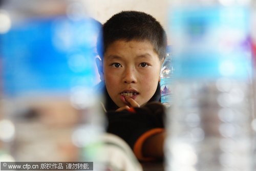 A boy looks at bottles of drinking water on a student's desk in Xundian autonomous county, in Southwest China's Yunnan province on March 31, 2010. [CFP]