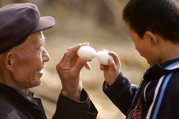 An aged local plays a traditional game of egg collision with his grandson in Heze, east China's Shandong Province, April 5, 2010. It is a local tradition to knock boiled eggs against each other on Qingming, the Tomb Sweeping Day, which falls on April 5 this year. One loses when his/her egg is cracked. [Xinhua]