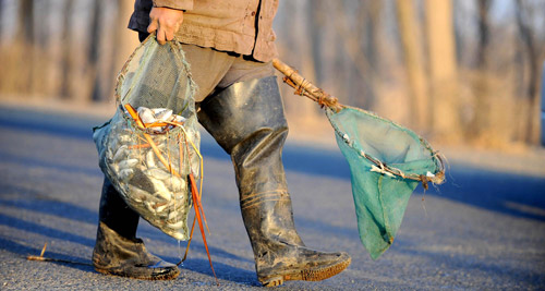 A farmer carries dead fish picked up from a reservoir in Shenyang, capital of Northeast China's Liaoning province, April 6, 2010. [Photo: Xinhua]