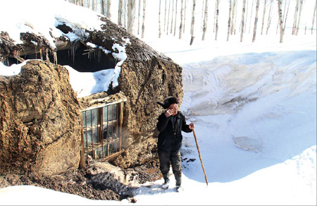 This photo taken March 29 shows 66-year-old farmer Zhang Haisheng in Wuxuete village, Xinjiang, in front of his adobe house whose roof had collapsed under the weight of snow. [China Daily]