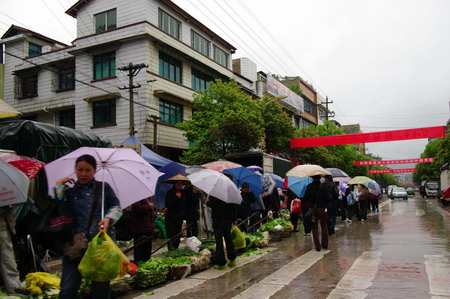 Residents hold umbrellas to buy vegetables in Fuquan city in southwest China's Guizhou province on April 13. The province welcomed a heavy rainfall Monday and Tuesday after an eight-month record drought. [Photo/Xinhua] 