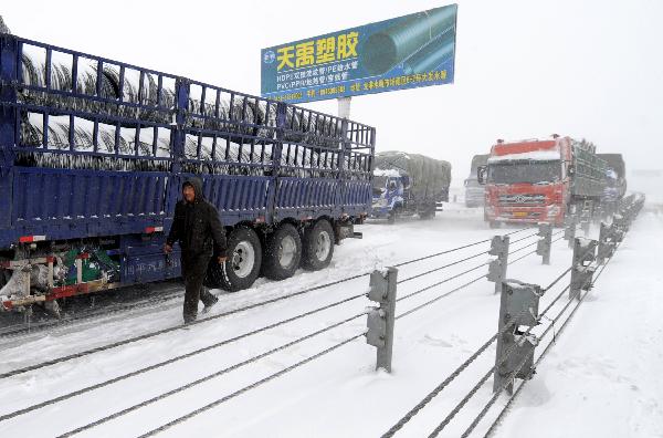 A driver walks by a truck, which has been trapped on the highway from Harbin to Tongjiang, in Harbin, capital of northeast China&apos;s Heilongjiang Province, April 13, 2010. The capital city of Heilongjiang Province was hit by the biggest snowstorm of the year on Tuesday, with roads and air traffic disrupted and schools closed.[Xinhua]