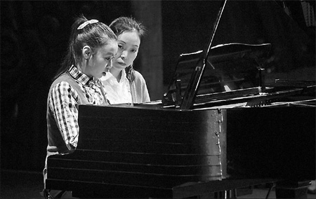 Ding Ziyin (left), a 16-year-old girl suffering from autism, plays the piano with her mother Lan Li sitting by. Ding Hao / for China Daily 