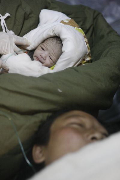 A newborn baby is seen with her mother at a makeshift shelter in Gyegu Town, Yushu County, northwest China's Qinghai Province, on April 17, 2010. [Shen Bohan/Xinhua]