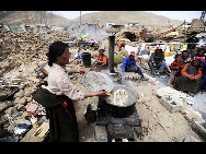 A Tibetan woman cooks noodles near the debris of collapsed buildings in the earthquake-hit town of Gyegu in Yushu County, Qinghai province, April 18, 2010. [Xinhua] 