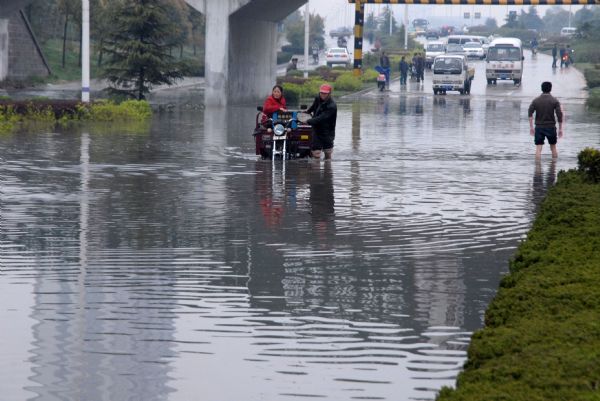  A couple manage to push their motor-tricycle through a flooded pass under a bridge after a sustaining rainfall since Saturday in downtown Huainan, southeast China's Anhui province, April 19, 2010.[Xinhua]