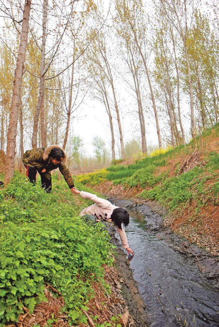 Tian Guirong, left, and a member from the Xinxiang Environmental Protection Volunteers, the NGO she set up in 2002, attempt to get water sample from a drainage outlet of a small pharmacy factory in Loucun, Henan province. [China Daily]