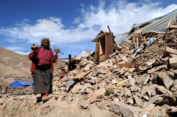 A local resident of China's Tibetan Ethnic Group turns the prayer wheel as she passes by debris in the quake-hit Gyegu Town of Yushu County, northwest China's Qinghai Province, April 20, 2010. 