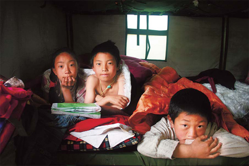   Three Tibetan children take cover under blankets for warmth in a temporary tent in Yushu county on Thursday. Heavy snow blanketed the county, posing challenges to relief eff orts and survivors.   