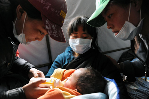 Two volunteers help a mother feed her injured baby in Yushu, Northwest China's Qinghai province on April 21, 2010.