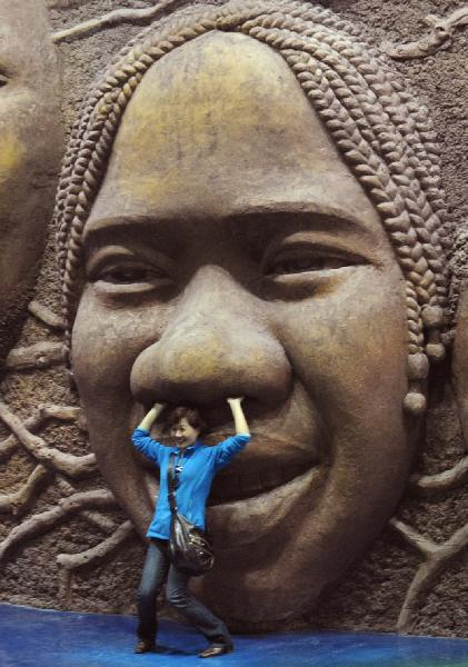 A visitor pose in front of the wall sculptured with laughing faces at African Pavilion in Shanghai Expo Park in Shanghai, east China, April 24, 2010. The Shanghai expo conducted trial operations for six times on April 20 - 26. [Xinhua/Wang Song]