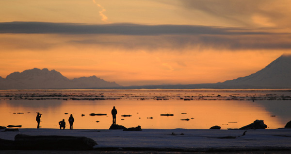 In this Friday night April 2, 2010 picture, people watch the sunset from the edge of the frozen mudflats near Elderberry Park in Anchorage, Alaska. The Mt. Spurr volcano is at right. 