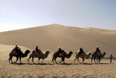 A group of tourists riding camels to enjoy the sightseeing of the Singing Sand Dunes, a popular tour resort in the subsurb of Dunhuang City, northwest China's Gansu Province, April 28, 2010. 