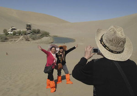 Three tourists take their souvenir photos with the backdrop of Crescent Moon Spring while enjoying the sightseeing of the Singing Sand Dunes, a popular tour resort in the subsurb of Dunhuang City, northwest China's Gansu Province, April 28, 2010. 