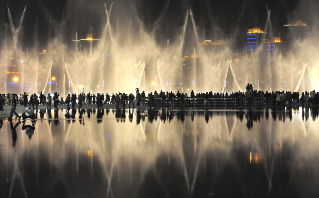 Visitors enjoy the performance of music fountain at the east bank of Huangpu River at the World Expo Park in Shanghai, east China, May 2, 2010. The night views of the World Expo Park with multicolored lights and various illumination effects give visitors different impression from the daytime. [Wang Song/Xinhua]