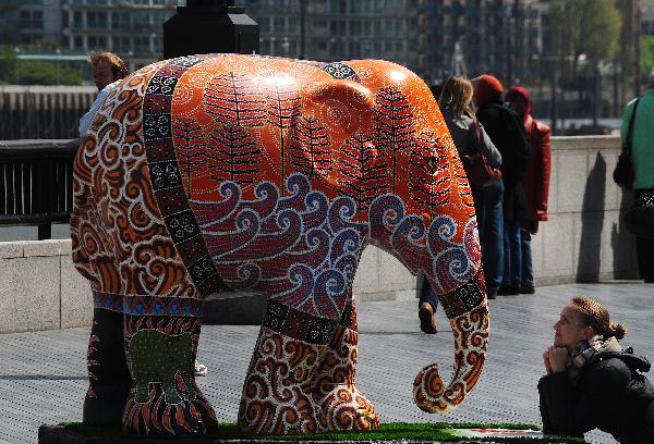 A tourist looks at a painted elephant sculpture near Tower Bridge in London, capital of Britain, May 5, 2010. Over 250 brightly painted life-size elephant sculptures have been located over central London recently. This is a conservation campaign that shines a multi-coloured spotlight on the urgent crisis faced by the endangered Asian elephant. The art works will be put into auction aiming to raise fund for the Asian elephants. [Xinhua/Zeng Yi] 